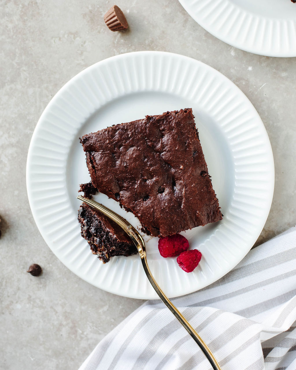 Slice of rich chocolate peanut butter  cake with melted Reese’s cups and chocolate chips, served on a white plate.