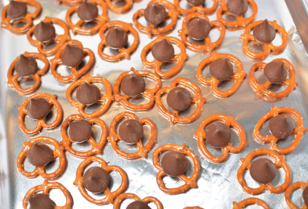 pretzels lined on a baking sheet with a hershey kiss in the center.