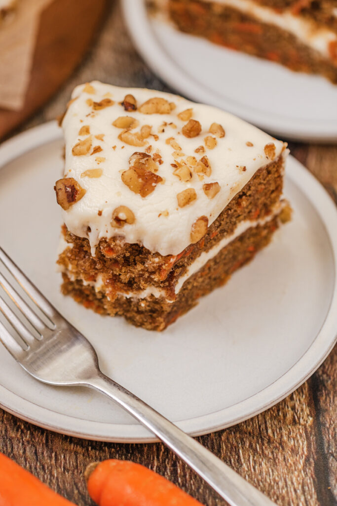 a serving of carrot cake on a cake plate with a fork.