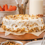 a cream cheese frosted carrot cake on a cake stand.