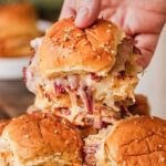 someone grabbing a Baked Reuben slider from a plate.