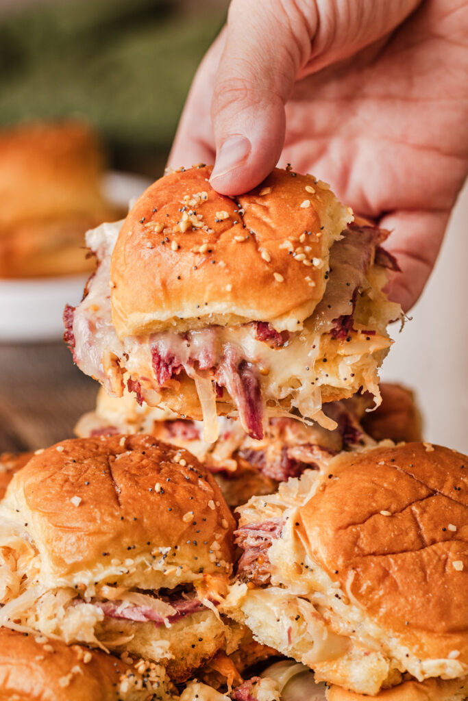 someone grabbing a Baked Reuben slider from a plate.