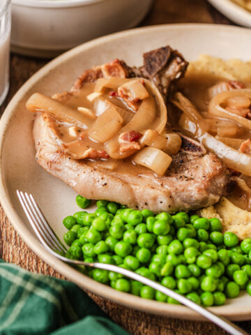 crockpot pork chops on a plate with sauteed onions and peas.