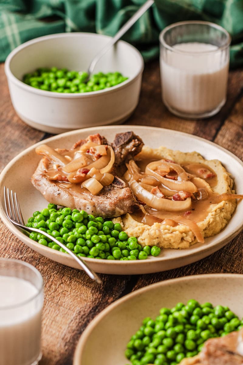 Crockpot smothered pork chops served on a plate with cooked peas.