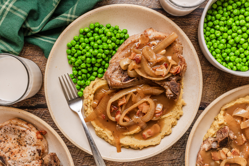 a serving of tender pork chops with potatoes and peas.