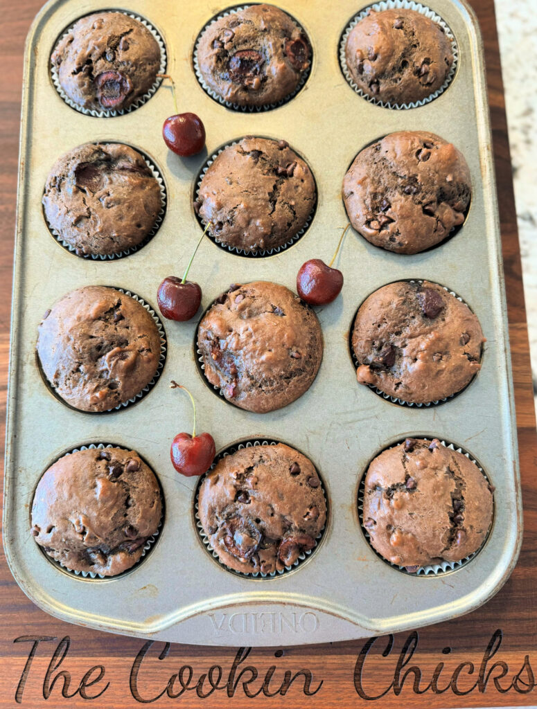 chocolate muffins with cherries throughout in a muffin pan.
