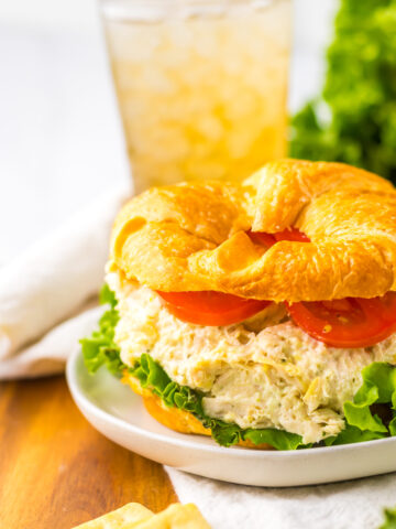 chicken salad served on a croissant on a plate with tomato and lettuce.