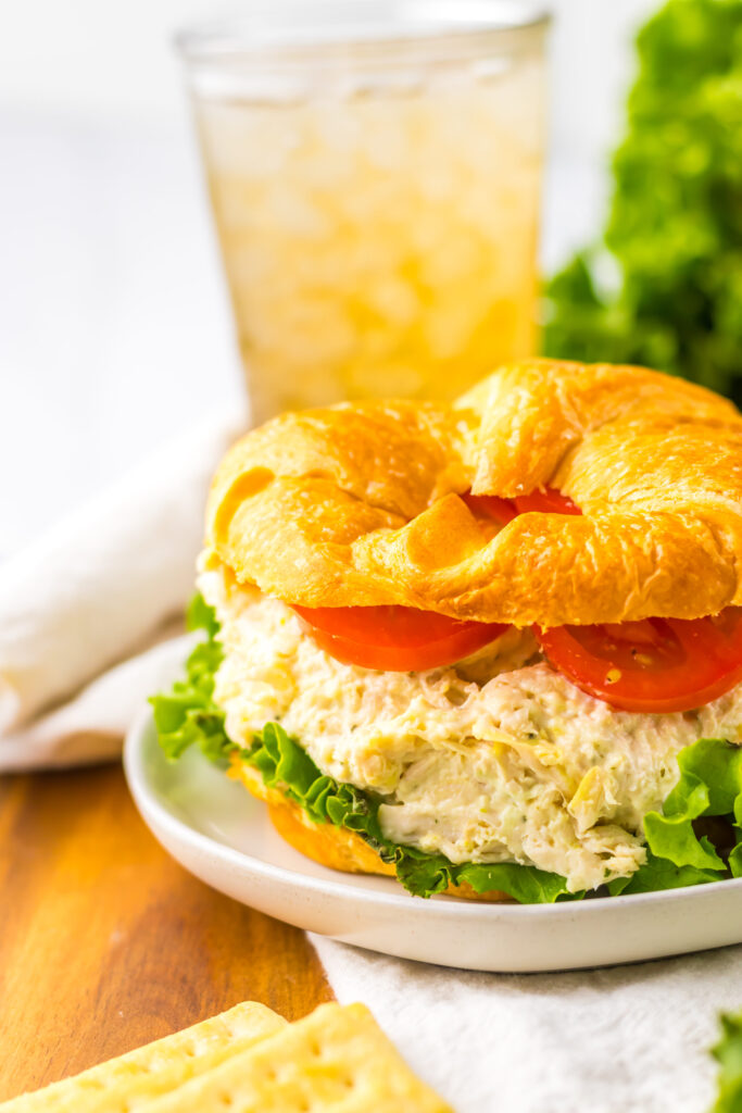 chicken salad served on a croissant on a plate with tomato and lettuce.