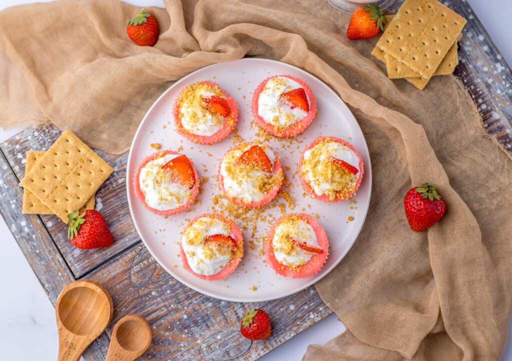 mini cheesecakes on a plate with whipped cream and crushed graham cracker crumbs.
