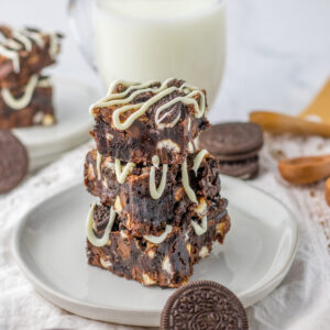 a baked and sliced stack of homemade brownies on a plate with a glass of milk.