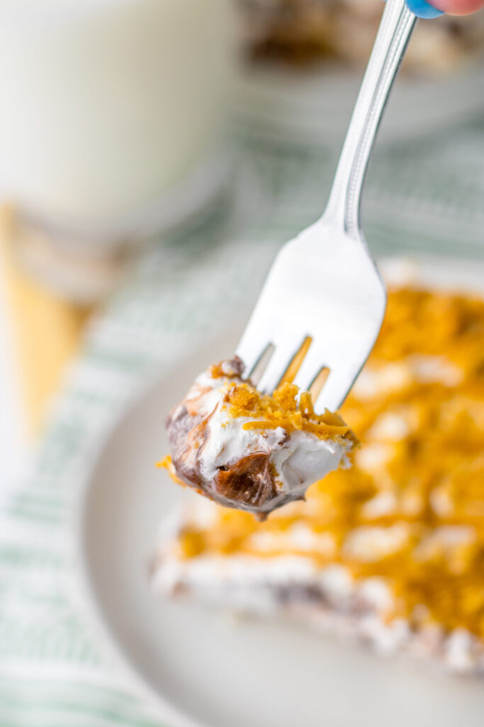 a fork taking a bite out of a piece of layered peanut butter and nutter butter cookie dessert.