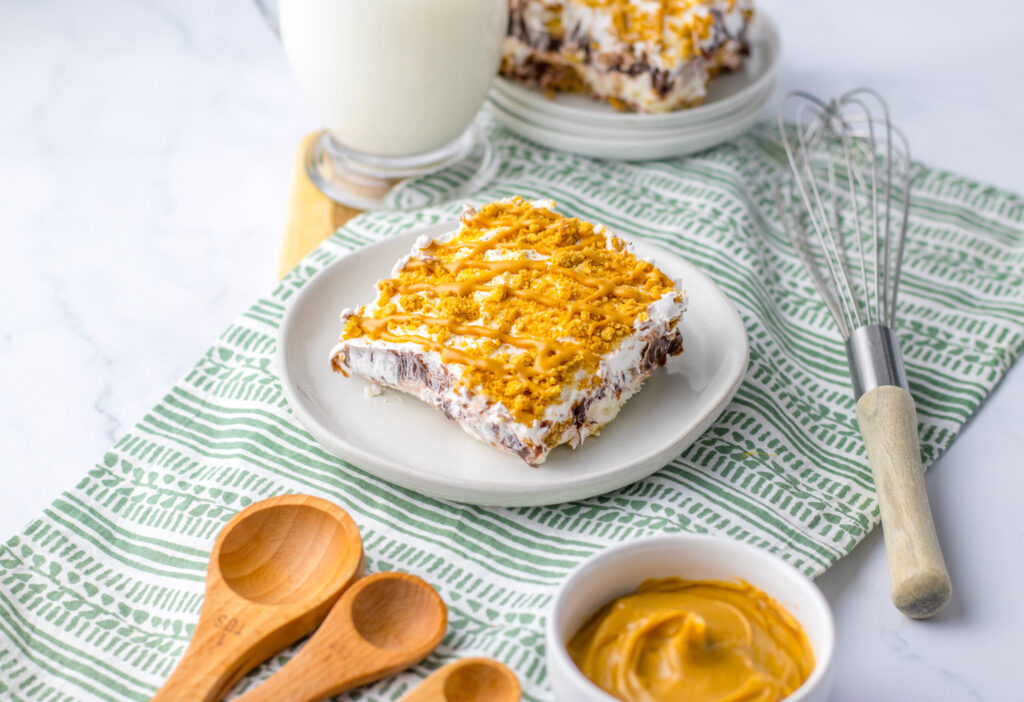a piece of layered peanut butter cookie lasagna on a plate with a glass of milk.