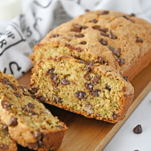 chocolate chips throughout a loaf of fresh zucchini bread on a cutting board.