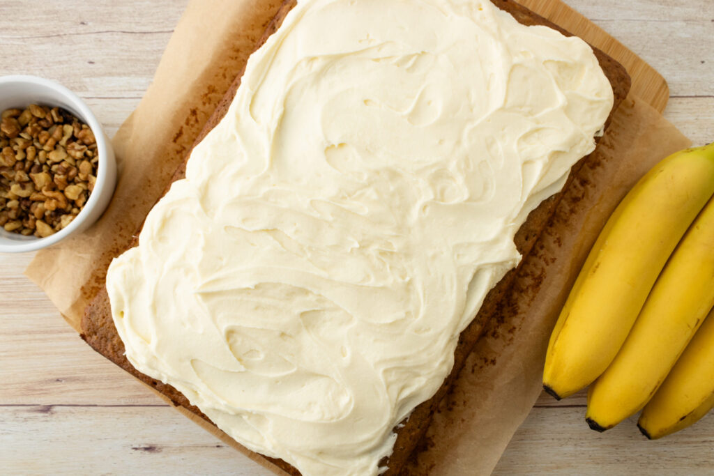 homemade cream cheese frosting spread on top of a banana bread cake.
