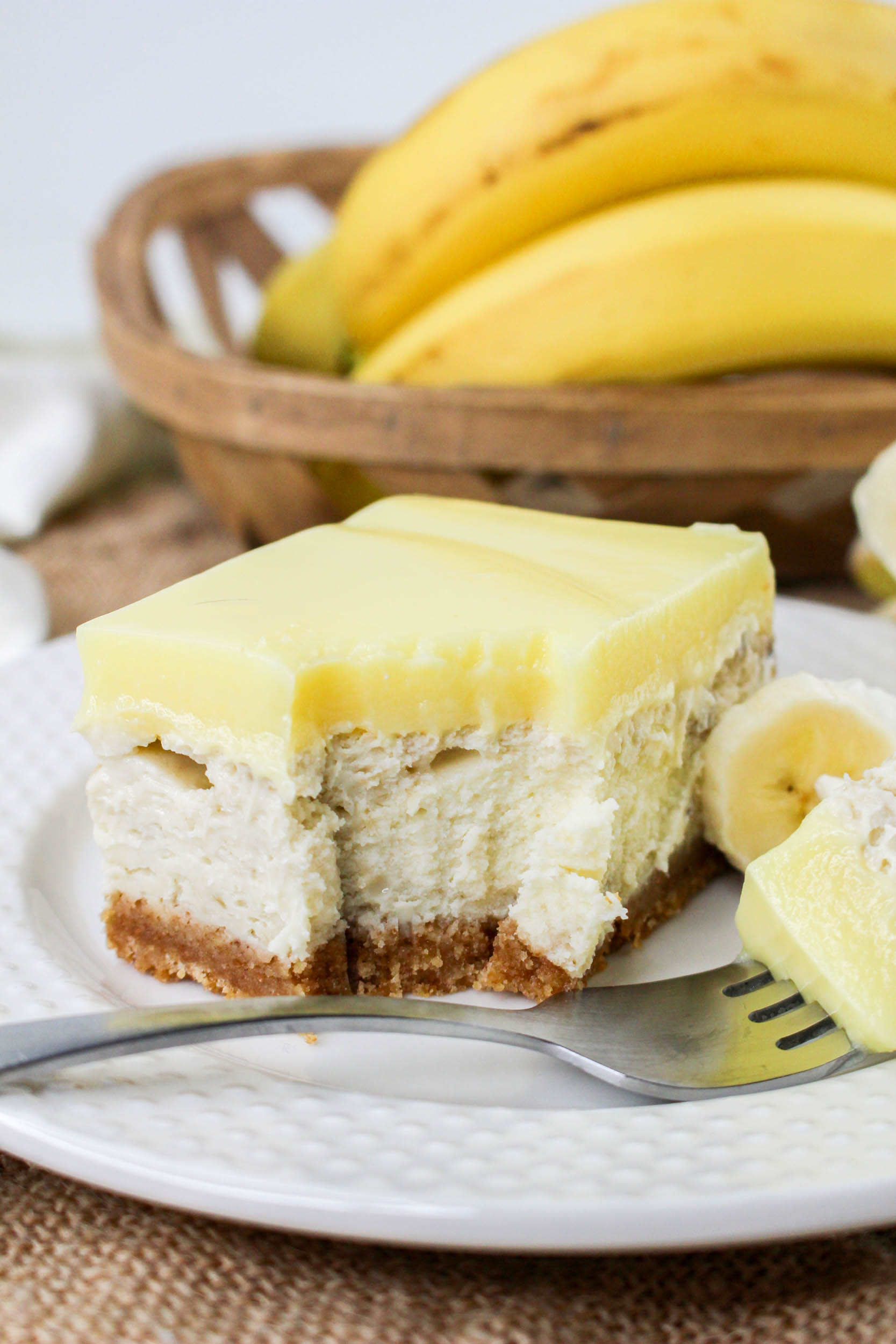 a banana pudding cheesecake square served on a plate with whipped cream and fresh slices of banana.