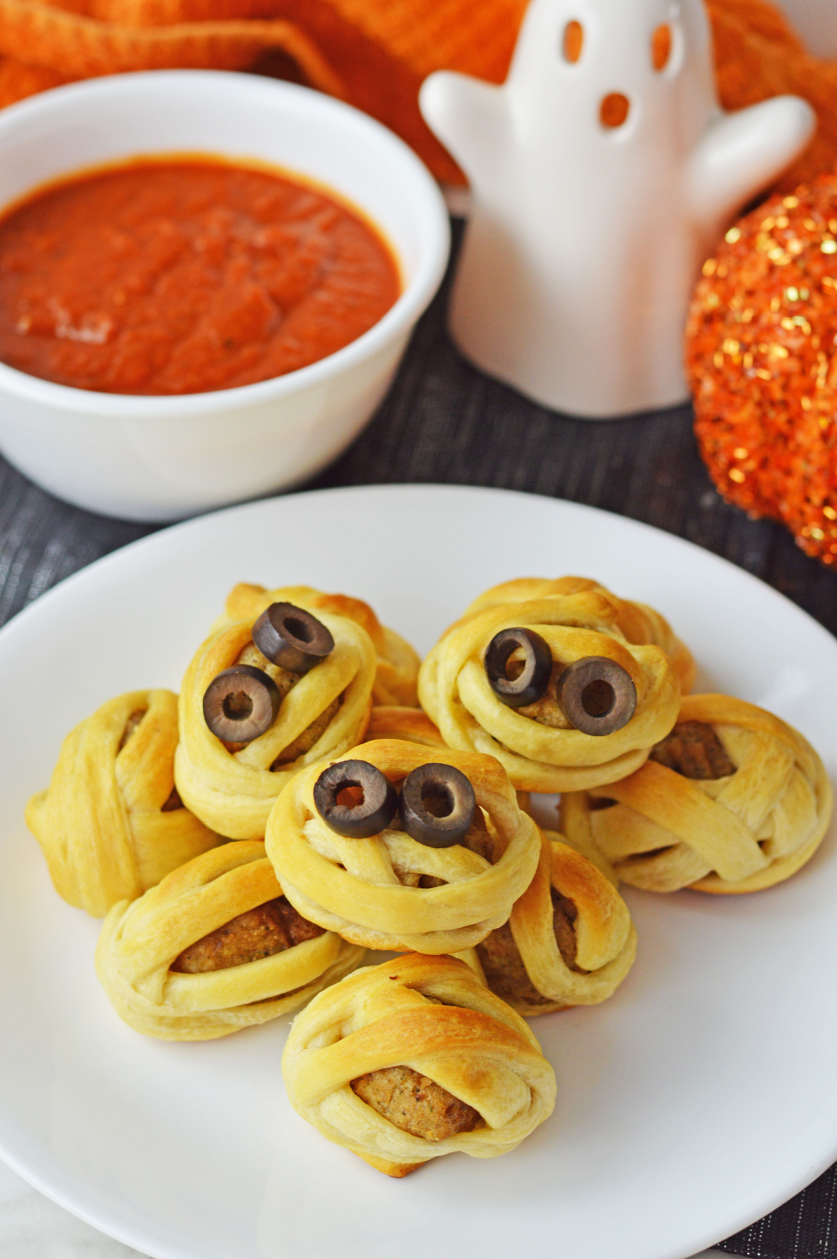baked mummy meatballs on a white serving plate.