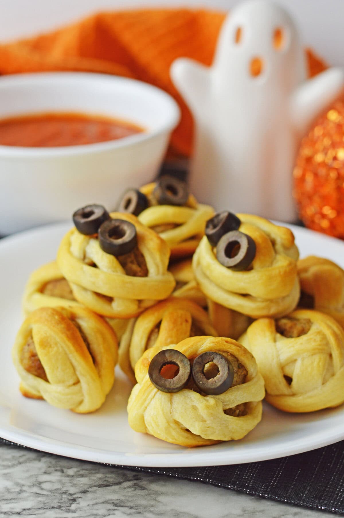 crescent roll wrapped meatballs with black olives on a white plate for Halloween.
