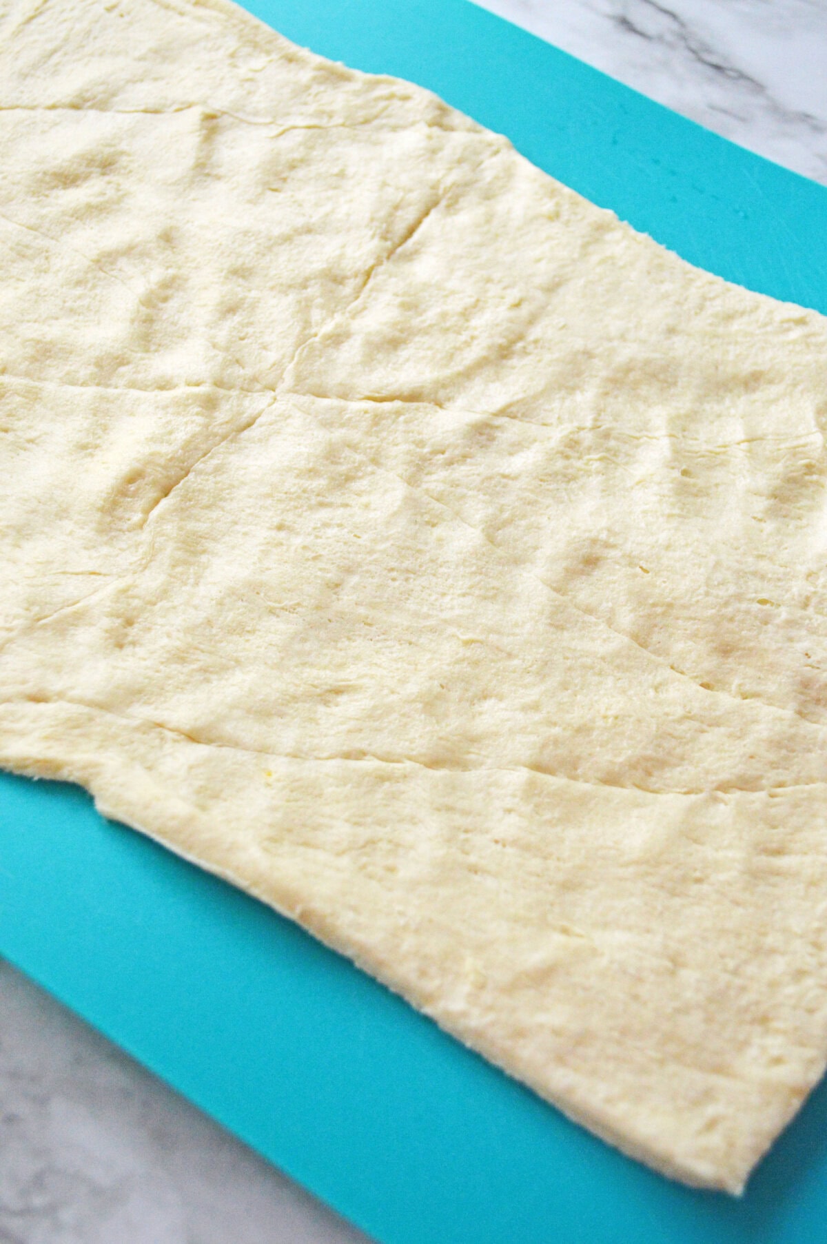 crescent dough rolled out to connect the seams on a cutting board.