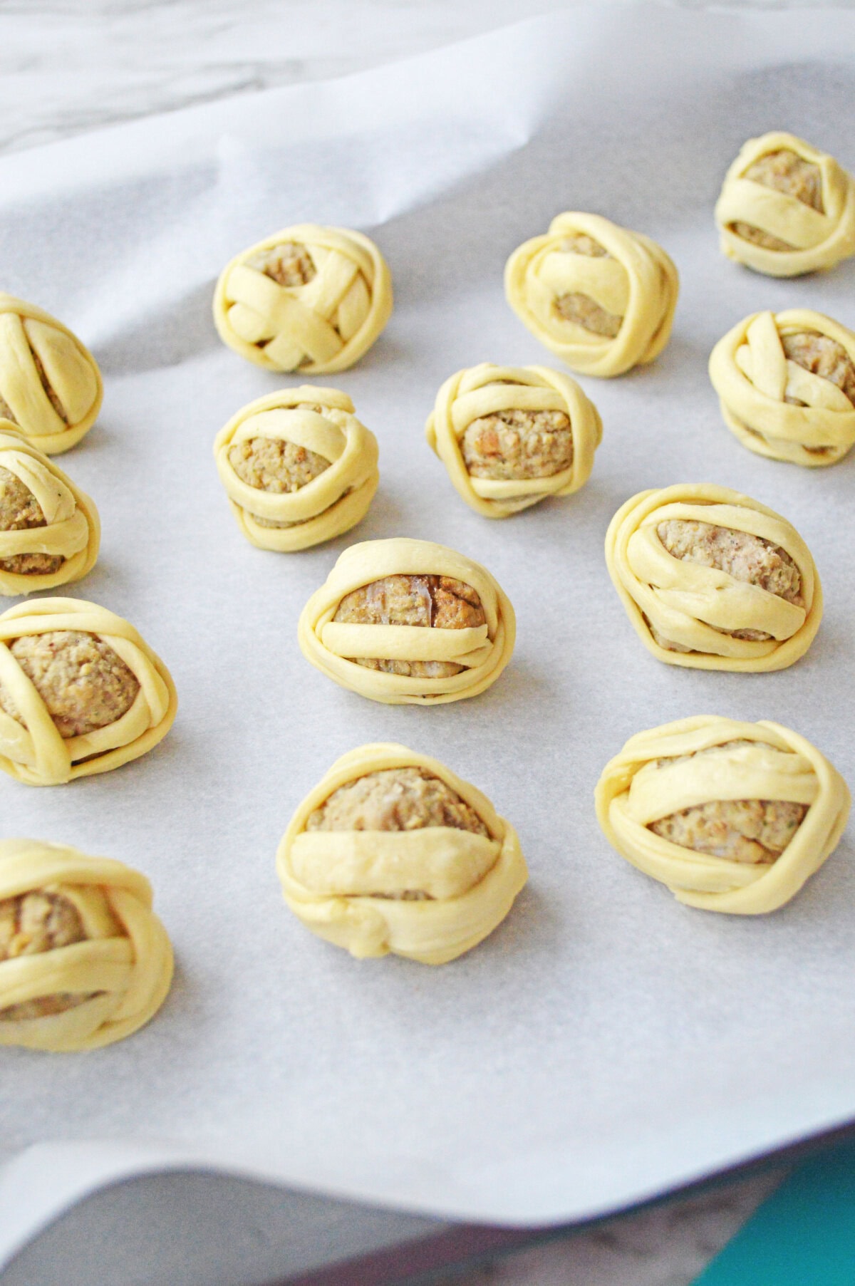 crescent roll dough wrapped around meatballs on a piece of parchment paper.