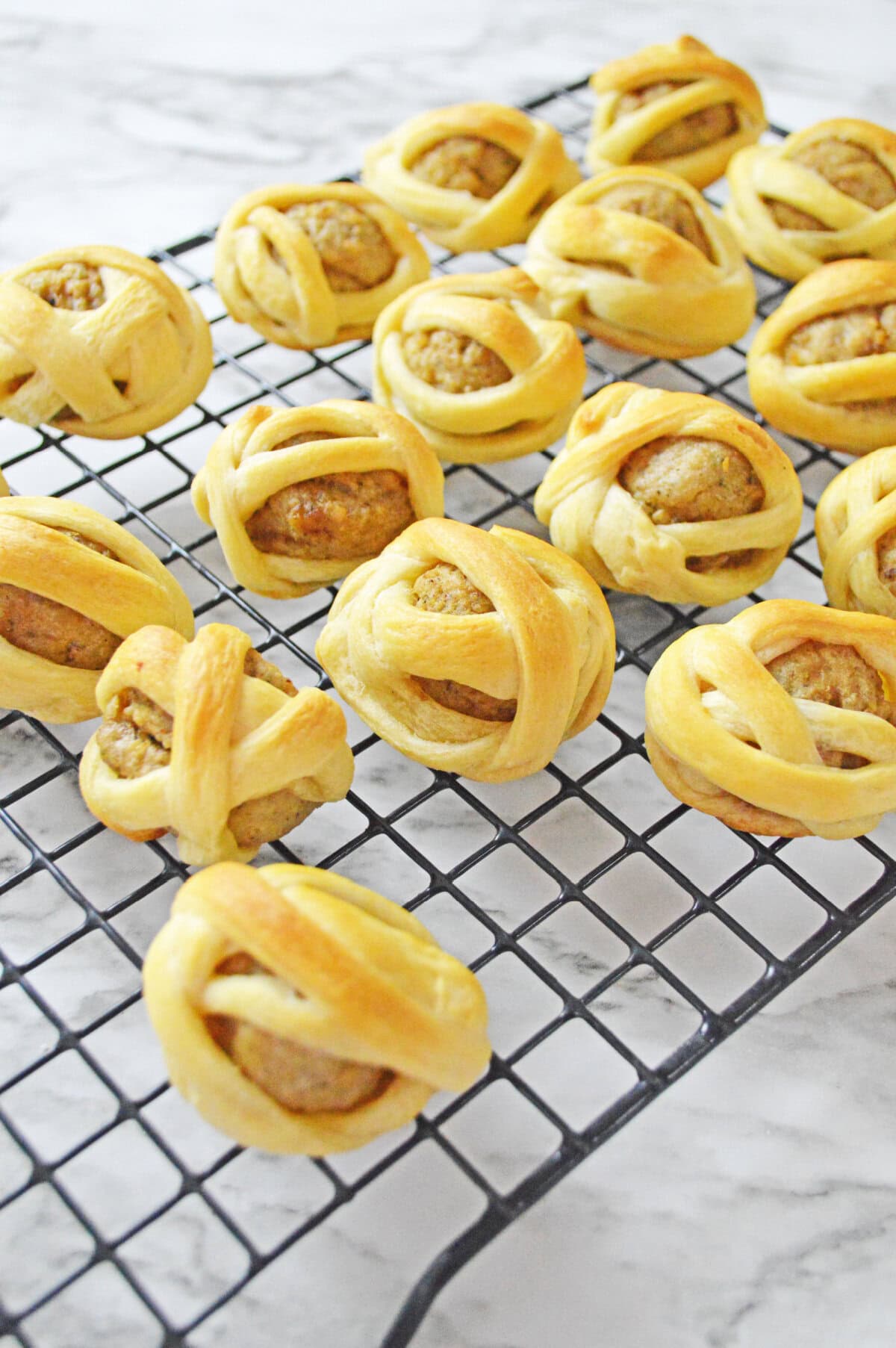 cooked crescent roll dough over meatballs cooling on a wire rack.