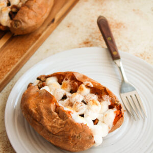 a sweet potato with marshmallow filling served on a white plate with a fork.