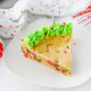 A slice of chocolate chip cookie cake with green frosting and m & m's.