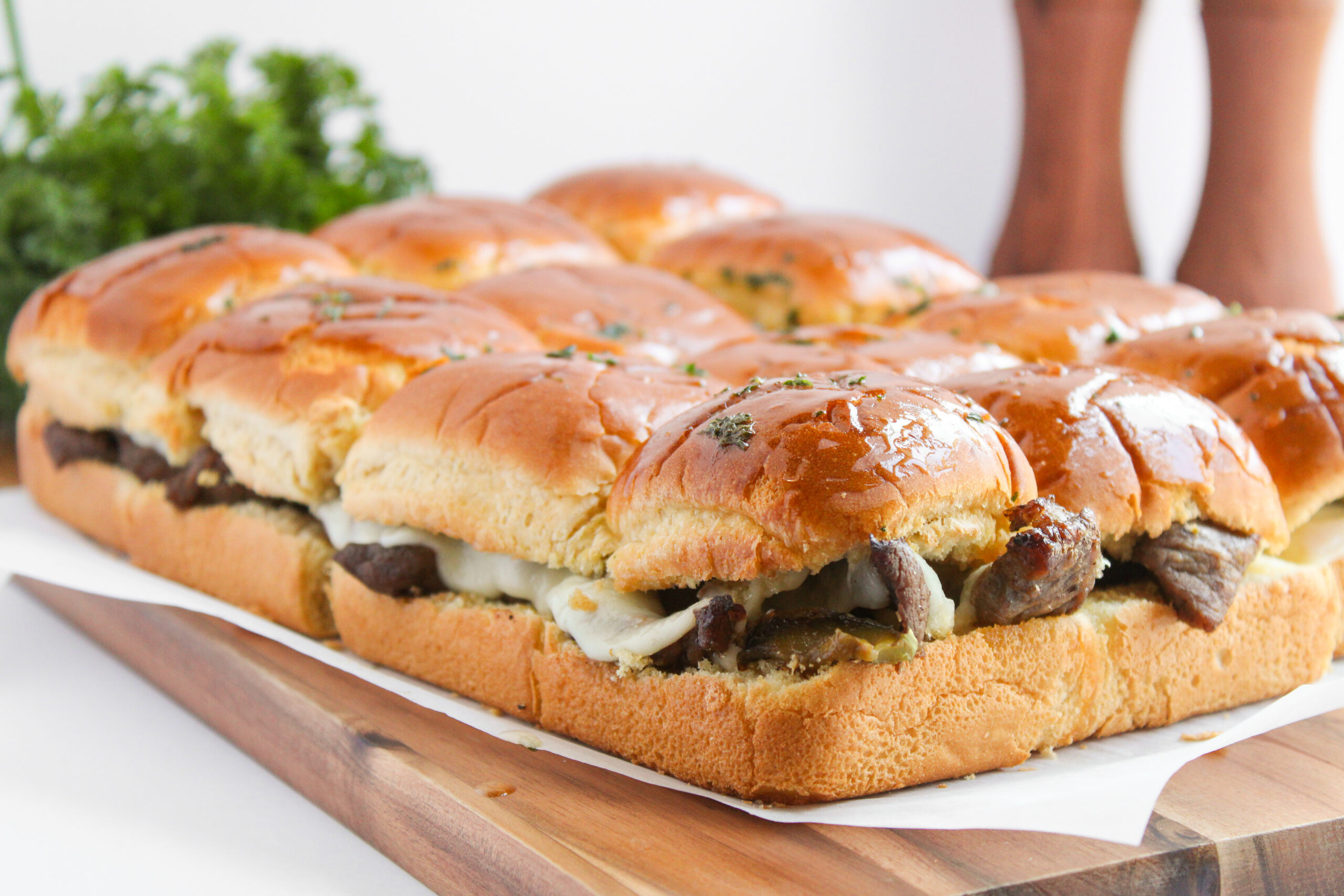 sandwich buns with ribeye steak, onions, peppers, and cheese on a wood board.