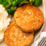 two salmon patties on a plate with broccoli.