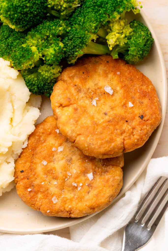 two salmon patties on a plate with broccoli.