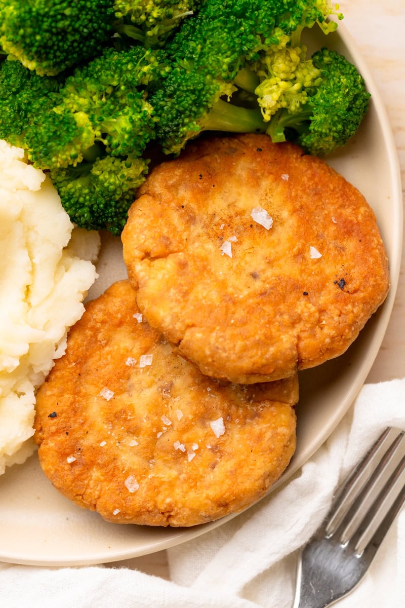 two salmon patties on a plate with broccoli.