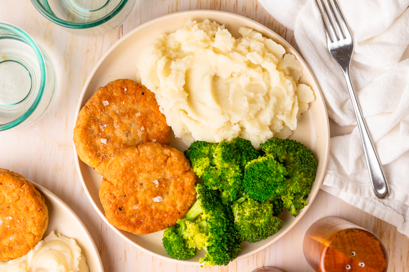 a plate of mashed potatoes, broccoli, and two salmon patties.