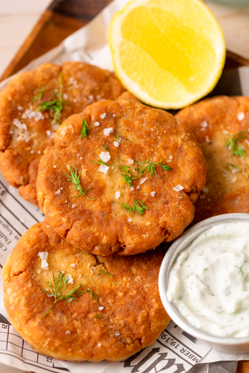 salmon patties served on a plate with tartar sauce and lemon.