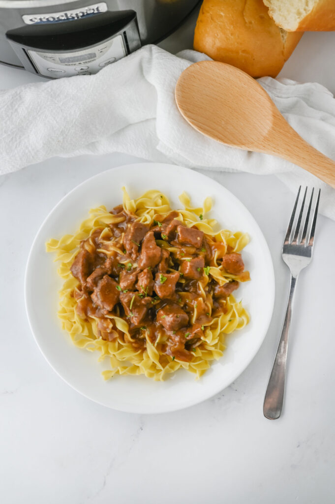 a white plate with egg noodles and tender steak tips.