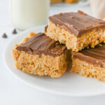 a peanut butter cereal bar with a chocolate layer stacked on a white plate.