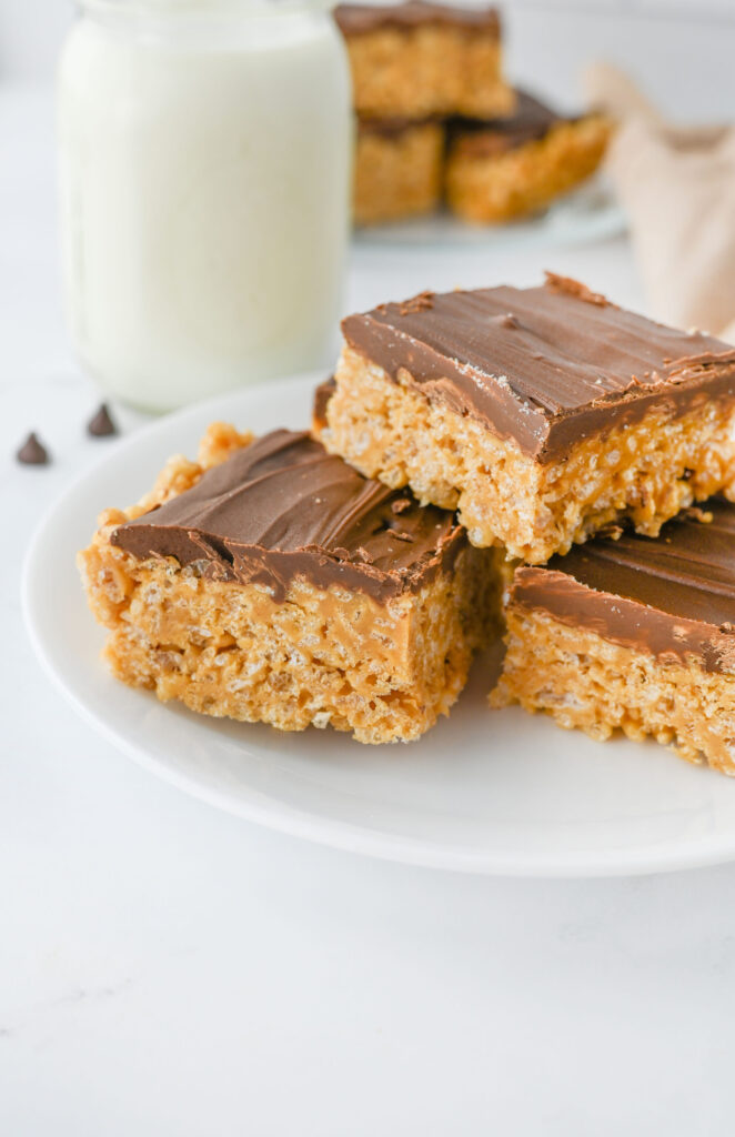 a peanut butter cereal bar with a chocolate layer stacked on a white plate.