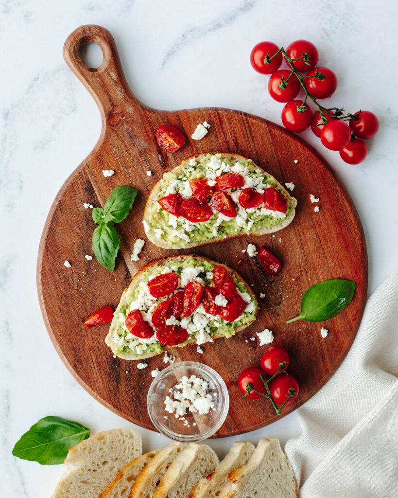 Avocado Toast with Tomato served on a wood circular board.