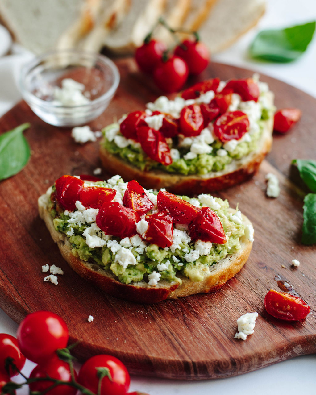 avocado toast with roasted tomatoes and feta on a wood board.