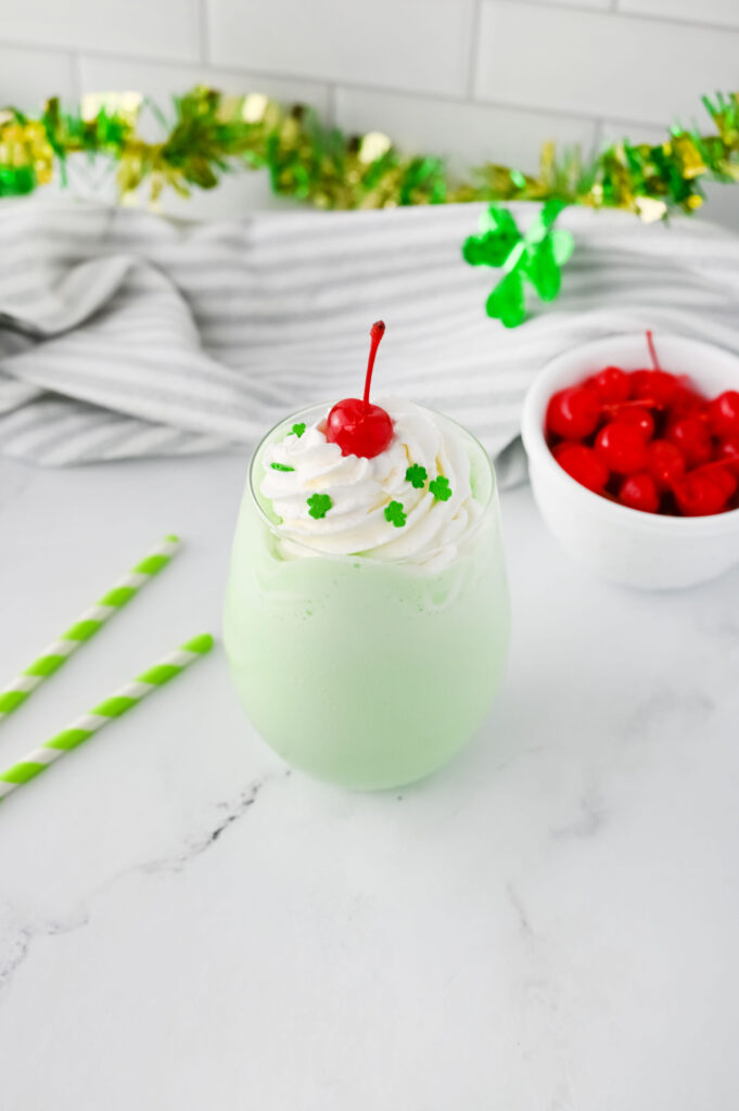 a mint green ice cream milkshake in a glass with whipped cream and a cherry.