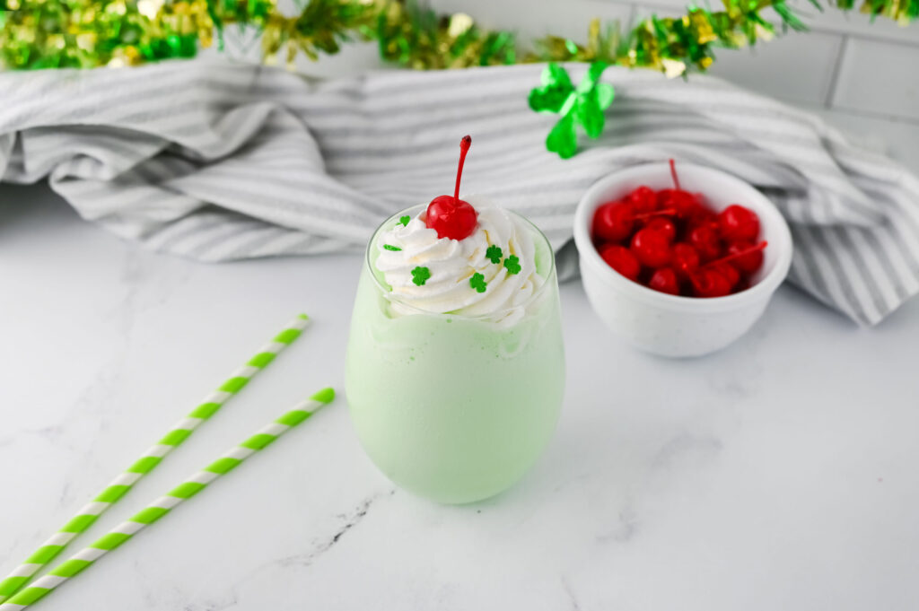 a creamy Shamrock Shake in a glass with whipped cream and a cherry.