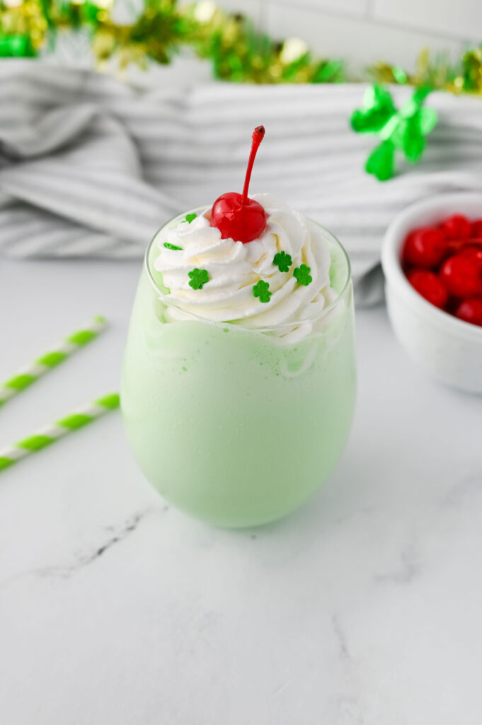 a minty ice cream drink served in a glass with whipped cream and a red cherry.