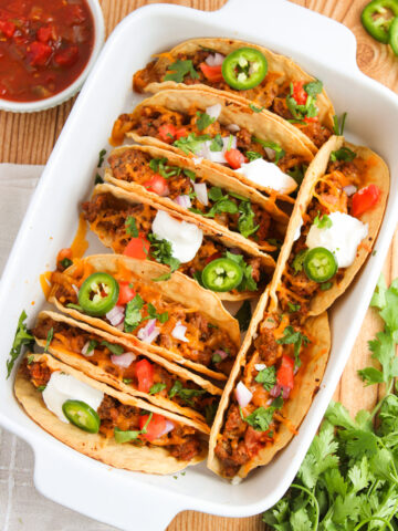 ground beef tacos lined in a baking dish with toppings.