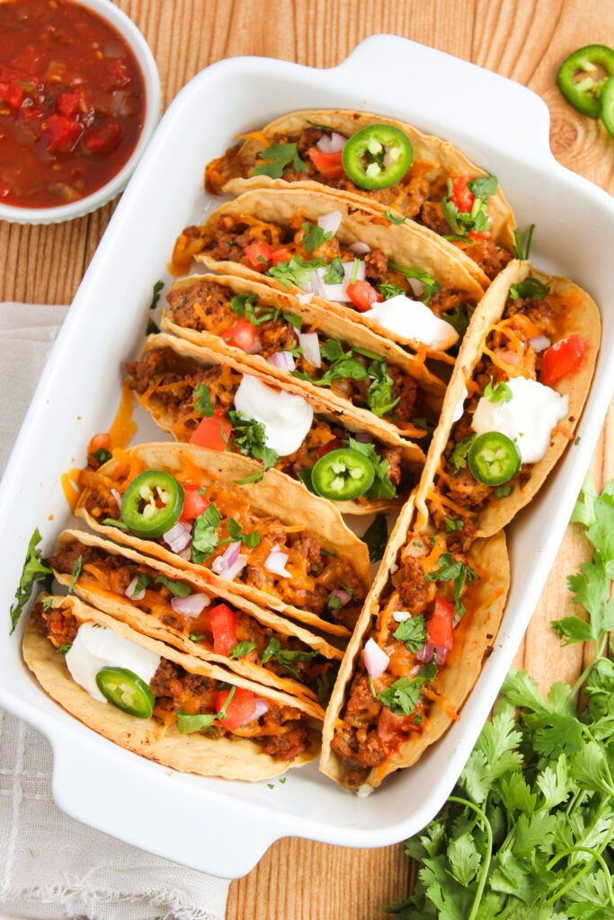 ground beef tacos lined in a baking dish with toppings.