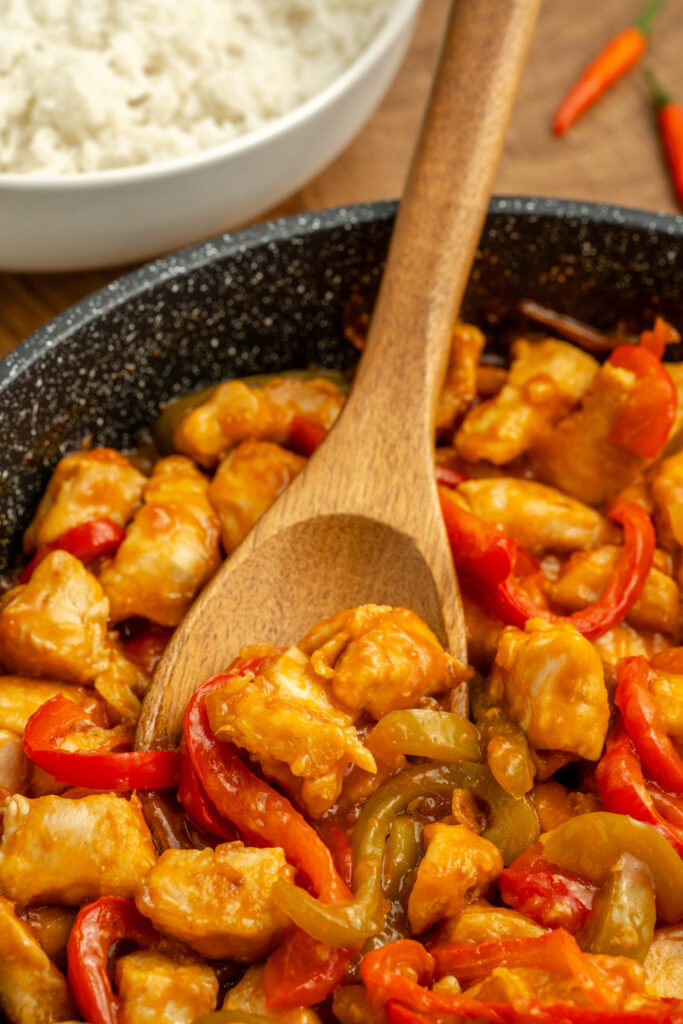 a sweet and spicy coated chicken in a skillet with peppers.