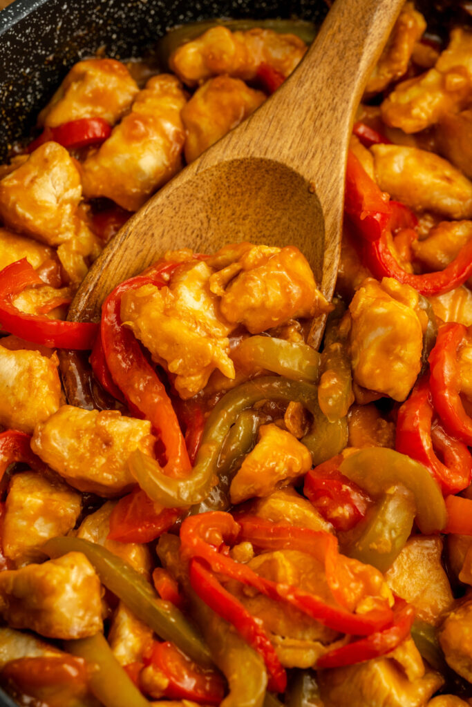 a wooden spoon scooping a spicy tomato coated chicken and peppers.