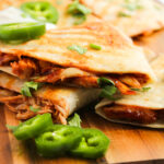 loaded tortillas with cheese and meat and topped with sour cream on a wood cutting board.