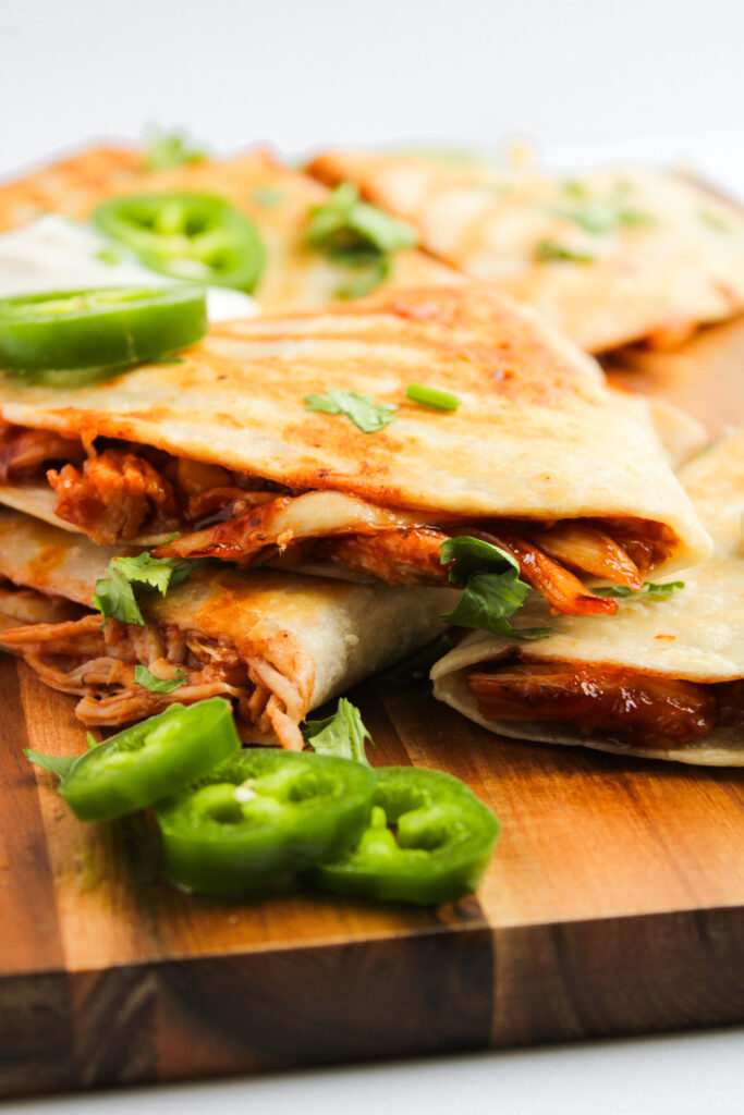 loaded tortillas with cheese and meat and topped with sour cream on a wood cutting board.