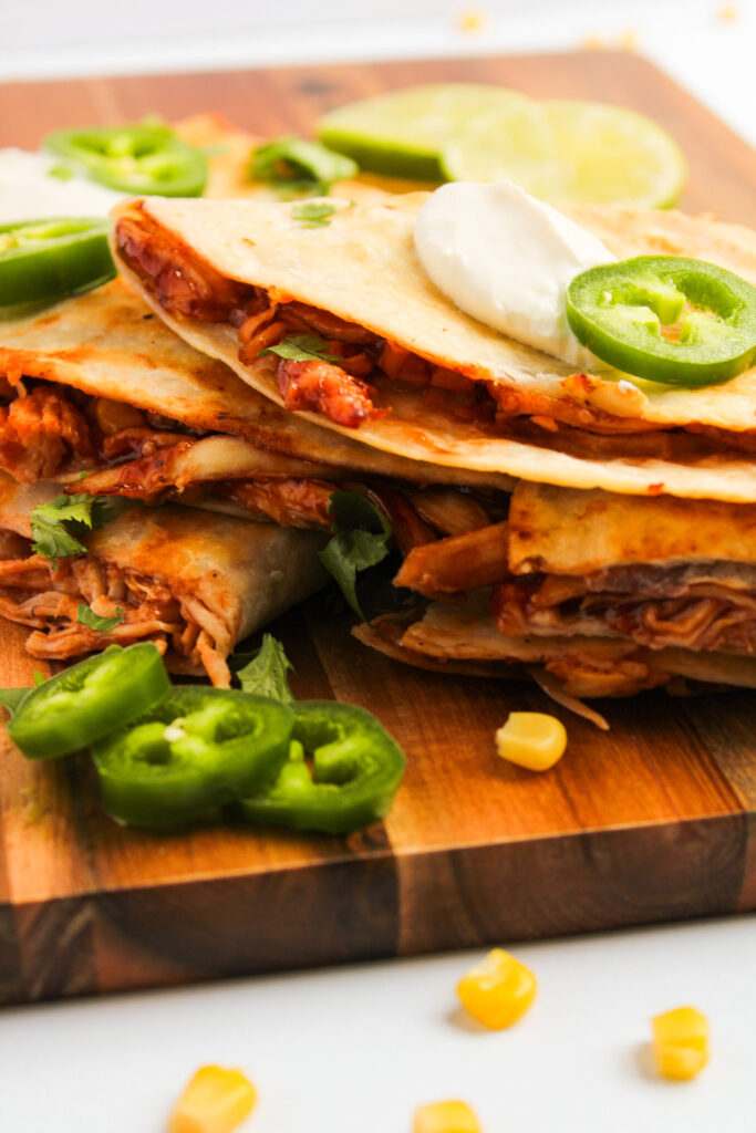 a BBQ seasoned chicken stuffed tortilla grilled and stacked on a wood board.