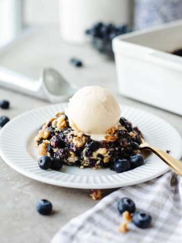 a white plate with a serving of dump cake with vanilla ice-cream on top.