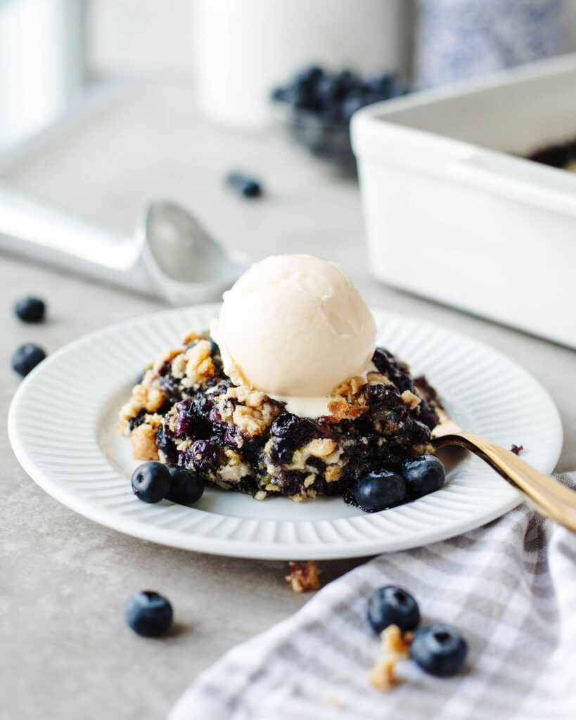 a white plate with a serving of dump cake with vanilla ice-cream on top.