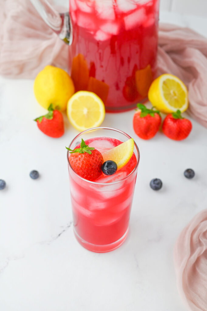 a garnished glass of Berry Lemonade with lemon wedges.